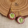 Handmade terracotta drop earrings featuring hand-painted green leaf motifs on a natural clay base.